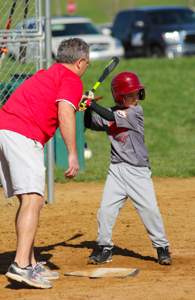 A boy plays little league baseball and is taught proper technique by his coach.