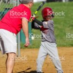 A boy plays little league baseball and is taught proper technique by his coach.